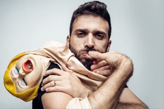 ארז בירנבוים מסתכל על המצלמה ומחזיק בידוי בובת מין